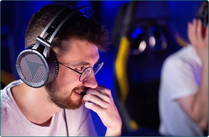 Een jongen met een koptelefoon zit voor de computer en glimlacht blij om zijn overwinning in het spel.