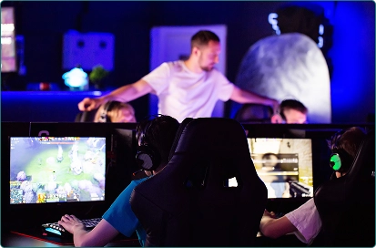 Het team van spelers zit achter computers en neemt deel aan het toernooi, de coach staat ernaast.